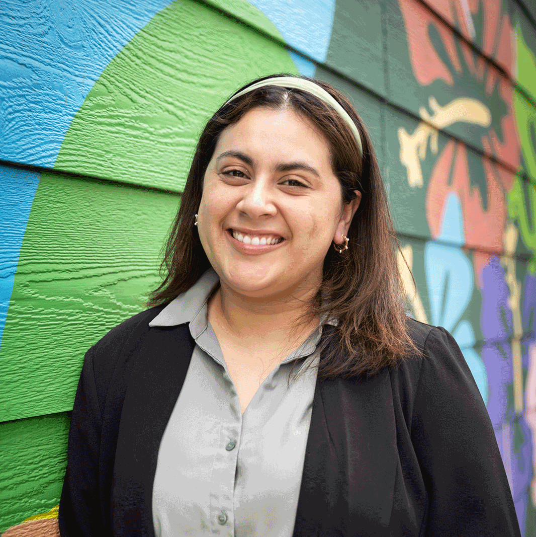 image of Adelante Legal team member Jennifer (Jenny) Rodriguez standing in front of a colorful mural